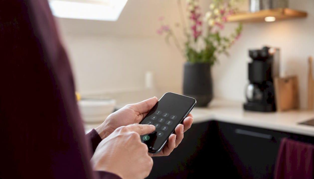 Een hand die van dichtbij een telefoonnummer intoetst op het toetsenbord van een mobiel.